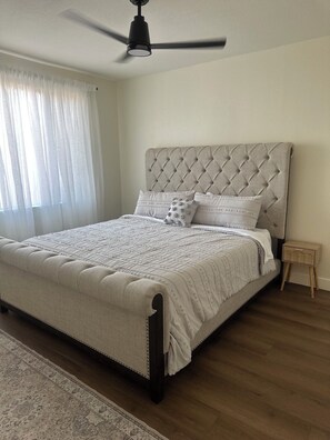 A bedroom with a tufted headboard, a bed with a quilted bedspread, a wooden nightstand, and a ceiling fan.