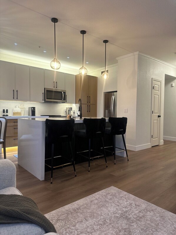 A modern kitchen with a central island, bar stools, and pendant lighting.
