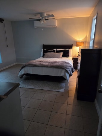 A bedroom with a bed, a ceiling fan, a nightstand, a lamp, and a dresser.. Cozy 1-bedroom studio in tranquil Lenoir City with AC