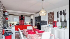 Una cucina moderna con tocchi rossi, un'area pranzo con tavolo rosso e una parete con posate e un calendario.