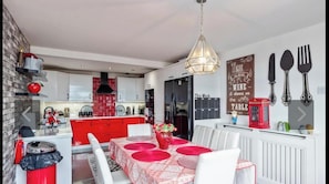 Una cocina moderna con detalles rojos, una zona de comedor con mesa roja, y una pared con cubiertos y un calendario.