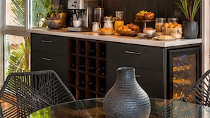 A modern kitchen with a glass dining table, dark cabinetry, and a coffee machine. - Ava 19 Adults Only Villa - Bed & Breakfast (Puerto Vallarta)