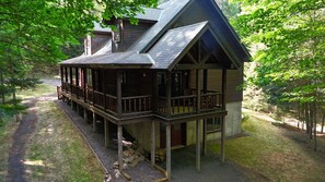 A wooden cabin with a porch, a chimney, and a stone foundation. - The Elkstone (Long Lake)