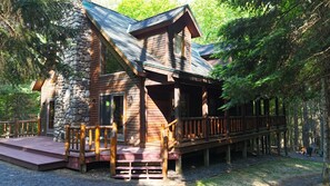 A cabin with a stone foundation, wooden exterior, and a deck with a railing. - The Elkstone (Long Lake)