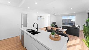 Una cocina moderna con una isla blanca, grifo negro y una zona de comedor con sofá negro y mesa de madera.