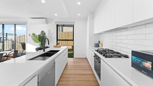 Una cocina moderna con armarios blancos, lavavajillas integrado, estufa a gas y un amplio ventanal con vista a un jardín.