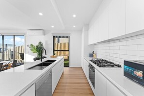Uma cozinha moderna com armários brancos, máquina de lavar louça embutida, fogão a gás e uma grande janela com vista para um jardim.