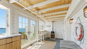 Une pièce avec un plafond en bois, des murs blancs, une grande fenêtre, une cheminée et une vue sur la mer.