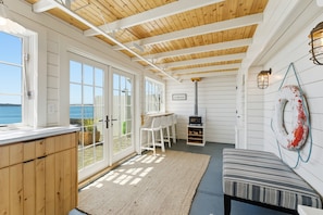 Ein Zimmer mit Holzbalkendecke, weißen Wänden, einem großen Fenster, einem Kamin und Blick aufs Meer.