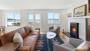 A living room with a sofa, armchair, coffee table, fireplace, and large windows overlooking the sea. - Perch - Waterfront Cabana | Puget Sound & Rainier Views (Seattle)