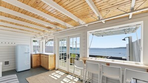 A kitchen with a view of the sea, wooden ceiling beams, and a white refrigerator. - Perch - Waterfront Cabana | Puget Sound & Rainier Views (Seattle)