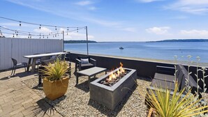 A patio with a fire pit, seating, and a view of the water. - Perch - Waterfront Cabana | Puget Sound & Rainier Views (Seattle)