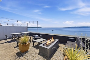 Eine Terrasse mit Feuerstelle, Sitzgelegenheiten und Blick auf das Wasser.