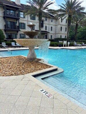 A pool with a fountain, lounge chairs, and a building with balconies in the background. - Recently updated Private resort style condo  (St. Augustine)