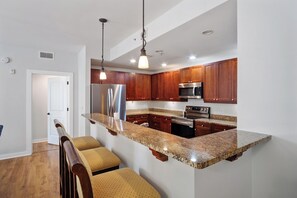 A modern kitchen with granite countertops, stainless steel appliances, wooden cabinets, and a bar seating area. - Recently updated Private resort style condo  (St. Augustine)