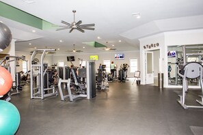 Ein Fitnessraum mit verschiedenen Trainingsgeräten, einem Deckenventilator und einem Schild mit der Aufschrift 'STUDIO'.