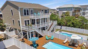 Ein zweistöckiges Haus mit einer Holzterrasse, einem Swimmingpool und einem eingezäunten Garten.