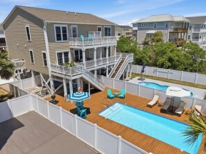Ein zweistöckiges Haus mit einer Holzterrasse, einem Swimmingpool und einem eingezäunten Garten.