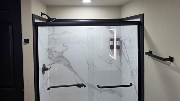Une douche entièrementClose avec un cadre noir, un revêtement mural imitant le marbre et une barre d'appui.