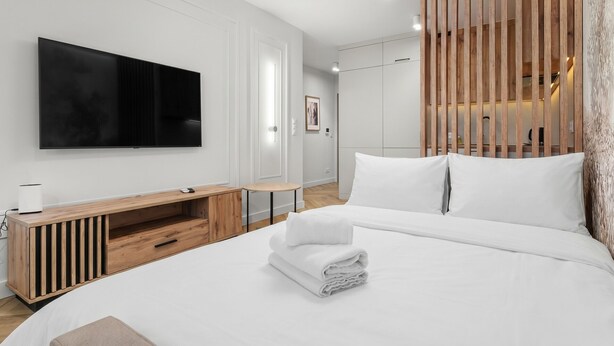 Ein modernes Hotelzimmer mit einem großen Bett, einem flachbildfernseher an der Wand, einem Holztischchen und einem großen Spiegel.