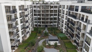 Ein mehrstöckiges Wohngebäude mit Balkonen, einem zentralen Innenhof mit Wegen und einer kleinen Grünfläche.