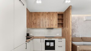 Eine kleine Küche mit Holzschränken, einem eingebauten Ofen und einem grauen Sofa im angrenzenden Wohnbereich.