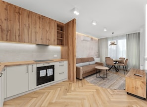 A modern kitchen with wooden cabinets, a built-in oven, and a dining area with a sofa and chairs. - City Łobzów Harmony Apartment (Kraków)