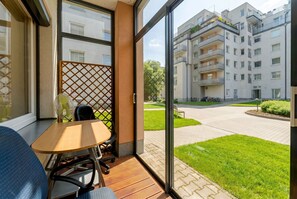 Een balkon met een tafel en stoelen, uitzicht op een woongebouw en een verzorgd gazon.