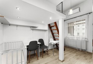 Een moderne, goed verlichte kamer met een wit plafond, houten vloer, een witte radiator, een raam met transparante gordijnen, een witte tafel met twee stoelen en een houten ladder.