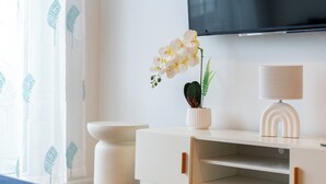 Ein modernes Zimmer mit einem weißen Schrank, einer Topf-Orchidee, einer Lampe und einem wandmontierten Flachbildfernseher.