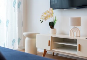 Una habitación moderna con un armario blanco, una orquídea en maceta, una lámpara y un televisor de pantalla plana en la pared.