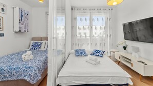 Ein Hotelzimmer mit Bett, Fernseher, Nachttisch und Fenster mit durchsichtigen Vorhängen.