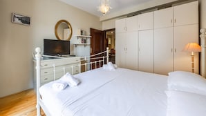 Une chambre à coucher avec un lit, une armoire blanche, une télévision et un miroir.