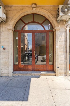 A building entrance with a large arched doorway, a motorbike parked outside, and an air conditioning unit on the wall. - Charming 1BR Apartment in Shkod r City Center (Shkodër)