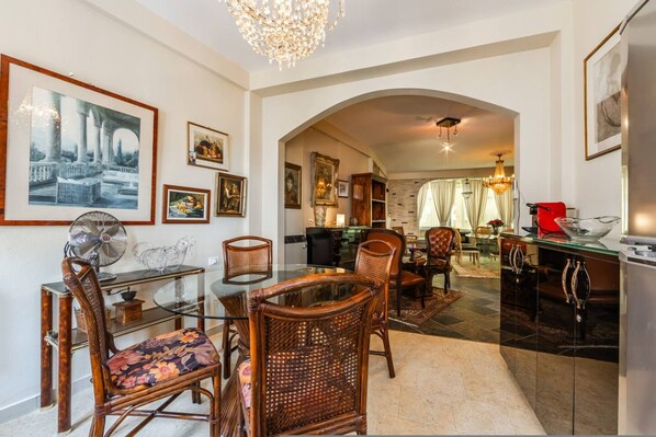 A dining area with wicker chairs, a glass table, and framed artwork on the walls. - Charming 1BR Apartment in Shkod r City Center (Shkodër)
