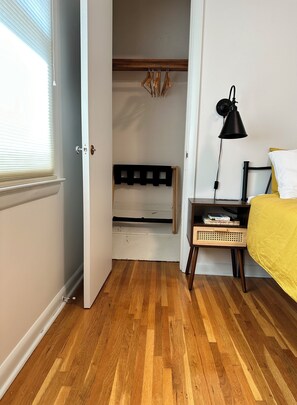 Ein Zimmer mit Holzboden, einem Bett mit gelber Bettdecke, einer schwarzen Schreibtischlampe und einem kleinen Tisch mit Büchern.