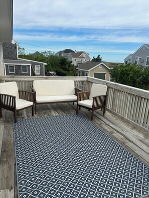 A wooden deck with a patterned rug, two white cushioned chairs, and a view of houses in the background. - The perfect family- and pet-friendly getaway steps from the sandy beach (Sandwich)