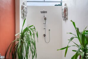 A shower with a handheld showerhead, a wall-mounted faucet, and a handheld showerhead. There are two large potted plants on either side of the shower. - A Cliff Residence Villa (Ubud)