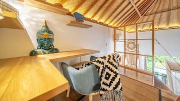 Una habitación con techo de madera, una estatua de Buda, una mesa, una silla y vistas a través de una ventana.