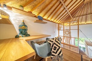 A room with a wooden ceiling, a Buddha statue, a table, a chair, and a view through a window. - A Cliff Residence Villa (Ubud)