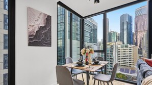 A dining area with a table set for two, a city view through large windows, and a modern interior design. - CBD-Edge 2BR | Pool, Gym, Sauna & City Views (West Melbourne)