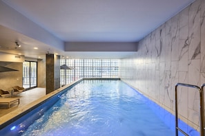 An indoor swimming pool with a clear view of the outside through large windows, a poolside seating area, and a modern interior design. - CBD-Edge 2BR | Pool, Gym, Sauna & City Views (West Melbourne)