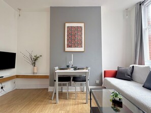 En moderne stue med spisebord, sofa, fjernsyn og et billede i ramme på væggen.