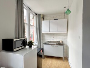 Et kompakt køkken med hvide skabe, en mikrobølgeovn og en lille vask.