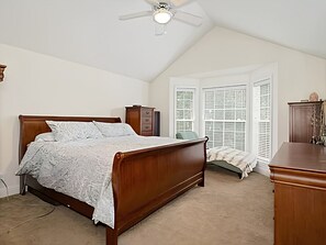 Un dormitorio con cama de madera, ventilador de techo, ventana con persianas y cómoda.