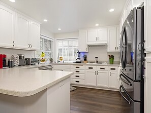 A modern kitchen with white cabinets, a large refrigerator, and a curved island.
