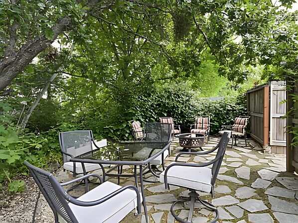 Eine Terrasse im Freien mit Steinböden, stahlrahmenartigen Stühlen und einem Glastisch.