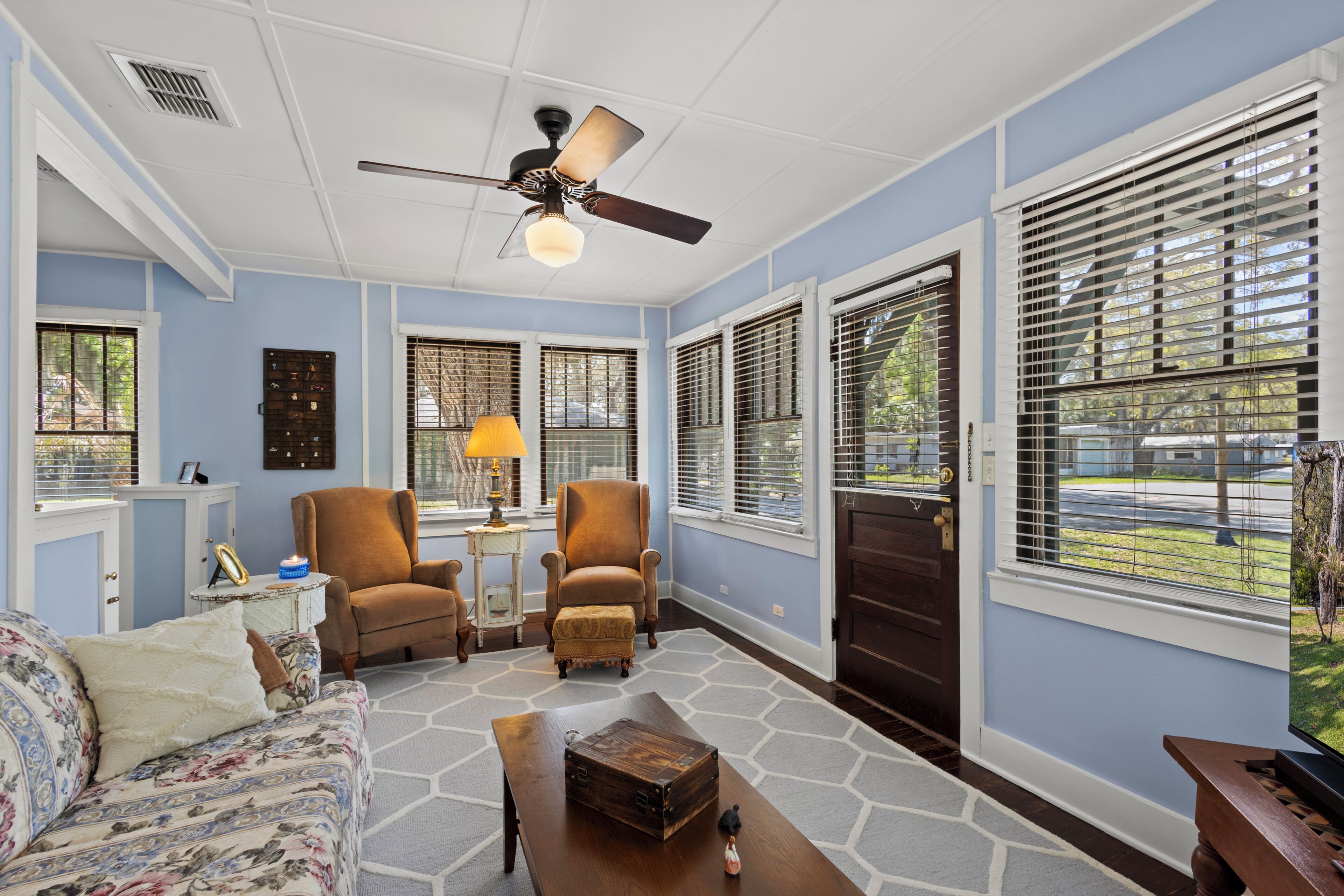 A room with a ceiling fan, two armchairs, a sofa, a coffee table, and a view through the window.