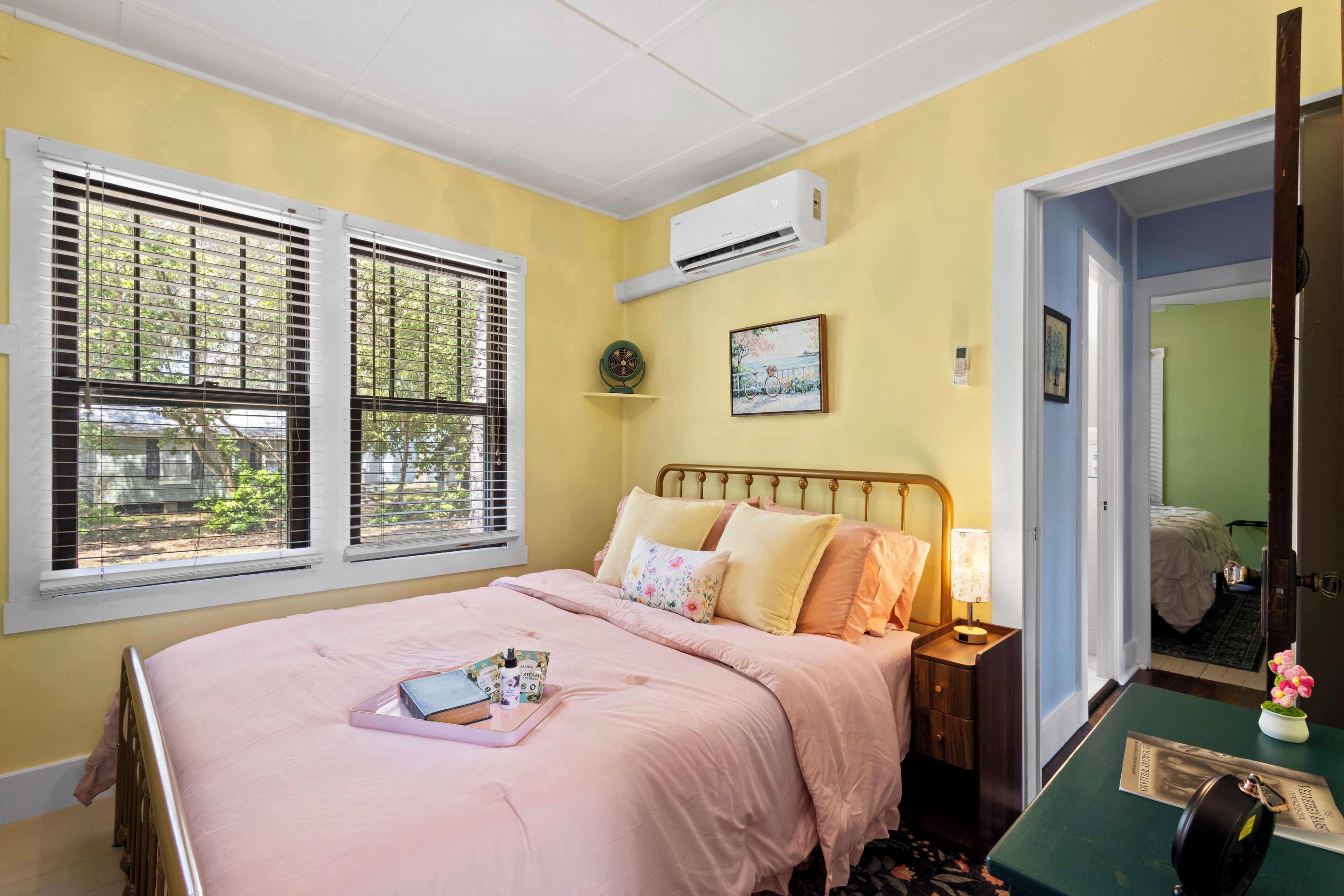 A bedroom with a bed, bedside table, lamp, and a window with blinds.
