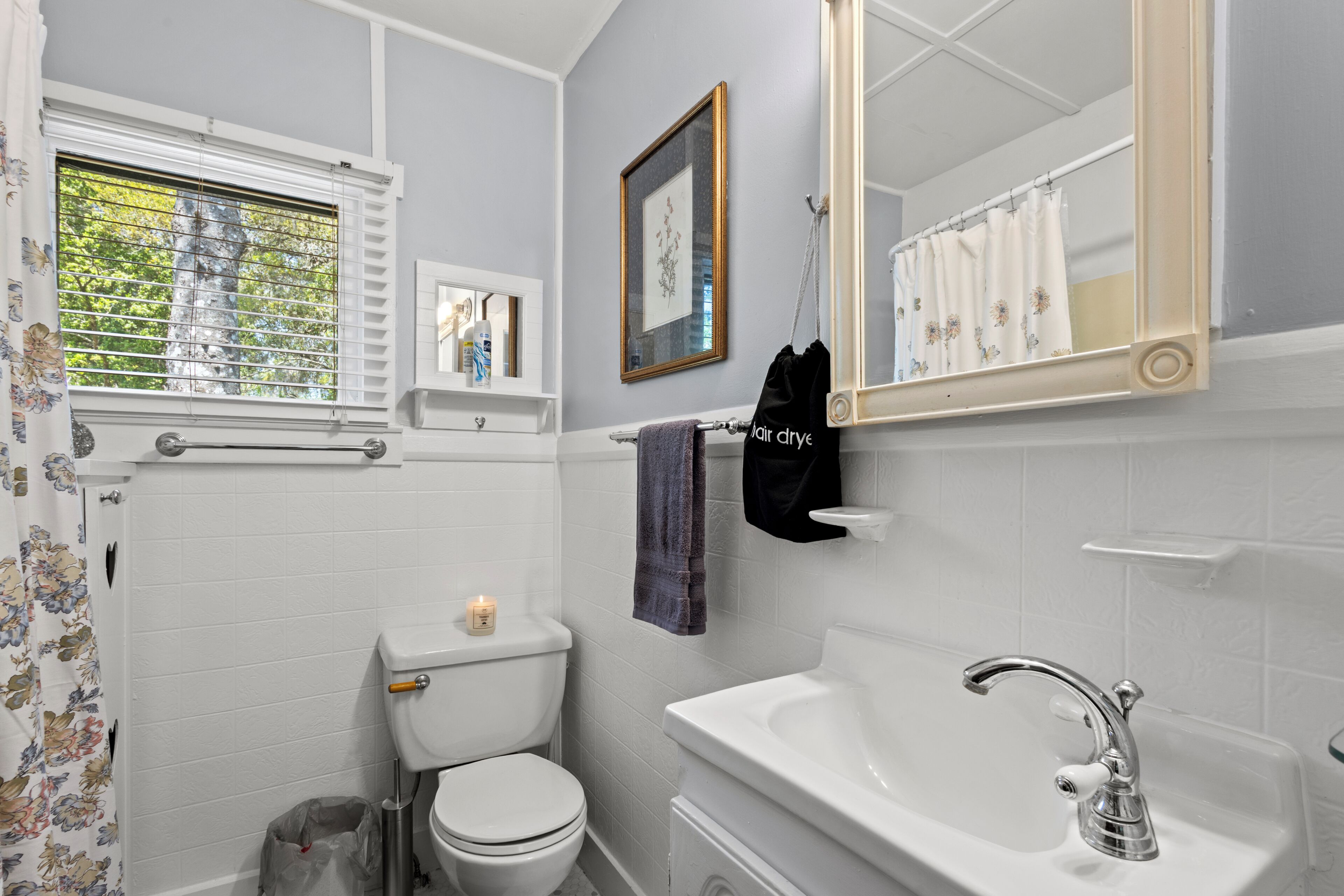 A bathroom with a toilet, sink, mirror, and window with blinds.